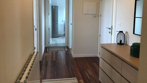 A hallway with wooden flooring, a kitchen in the background, and a bathroom door.