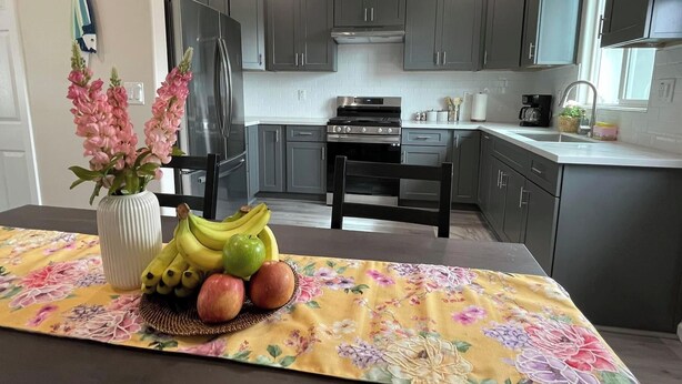 A modern kitchen with grey cabinets, a stainless steel refrigerator, and a dining area with a floral tablecloth.