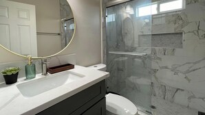 A modern bathroom with a marble shower wall, a round mirror, and a white sink.