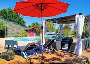 A poolside area with a red umbrella, lounge chairs, and a covered seating area.