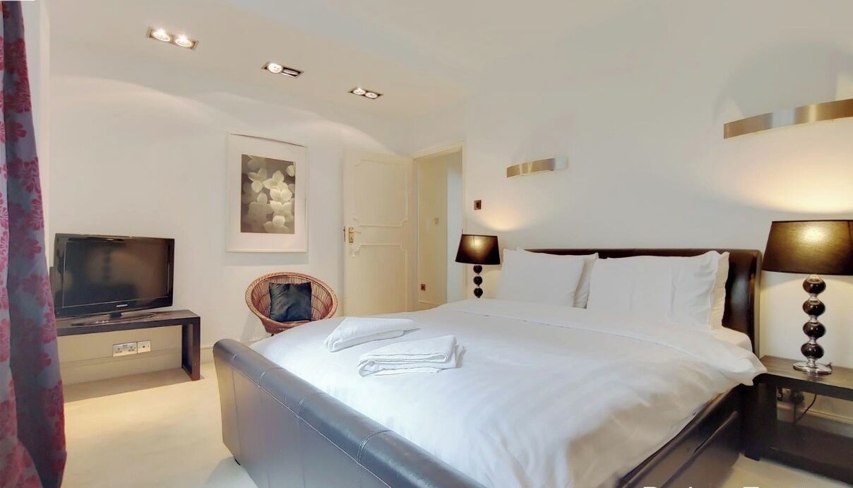 A hotel room with a bed, bedside lamps, a television, a chair, and a door.