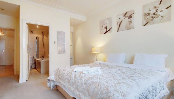 A hotel room with a large bed, a bathroom with a shower, and artwork on the walls.