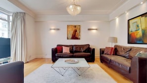 Ein Wohnzimmer mit zwei Ledersofas, einem Glastisch, einer Chandelüster und Kunstwerken an den Wänden.
