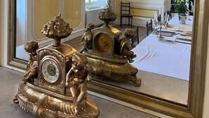 Een luxe kamer met gedetailleerd gouden meubilair, een grote spiegel die de kamer weerspiegelt, en een kroonluchter.