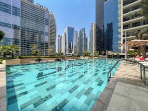 A swimming pool with a geometric tile pattern, surrounded by high-rise buildings and palm trees.