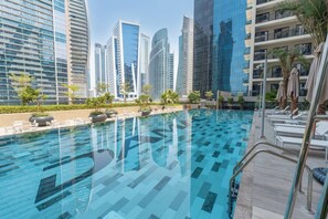 A swimming pool with lounge chairs and umbrellas, surrounded by high-rise buildings. - 1BR Retreat in Business Bay (Dubai)