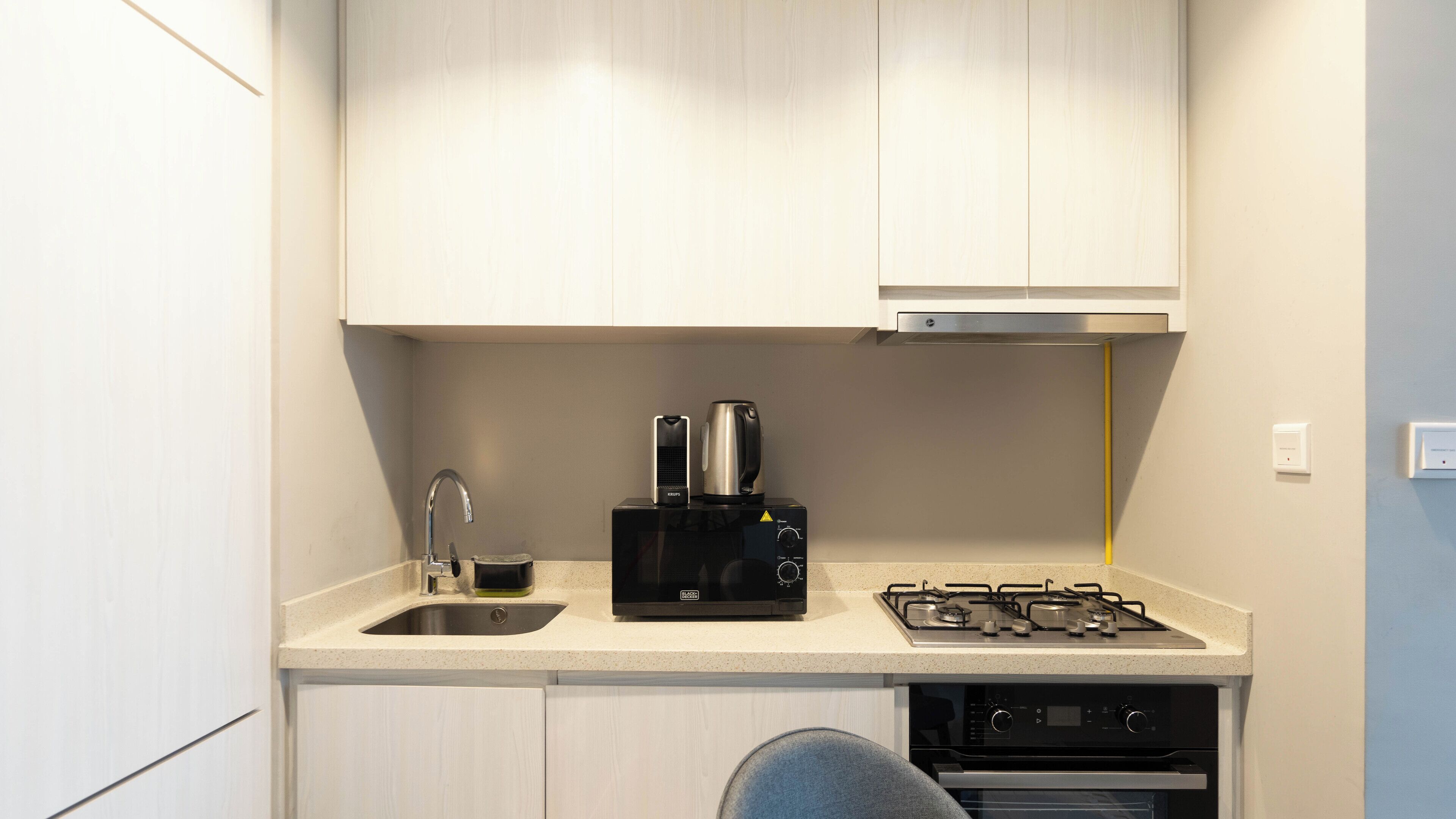A compact kitchenette with a sink, a coffee maker, a kettle, and a stove.