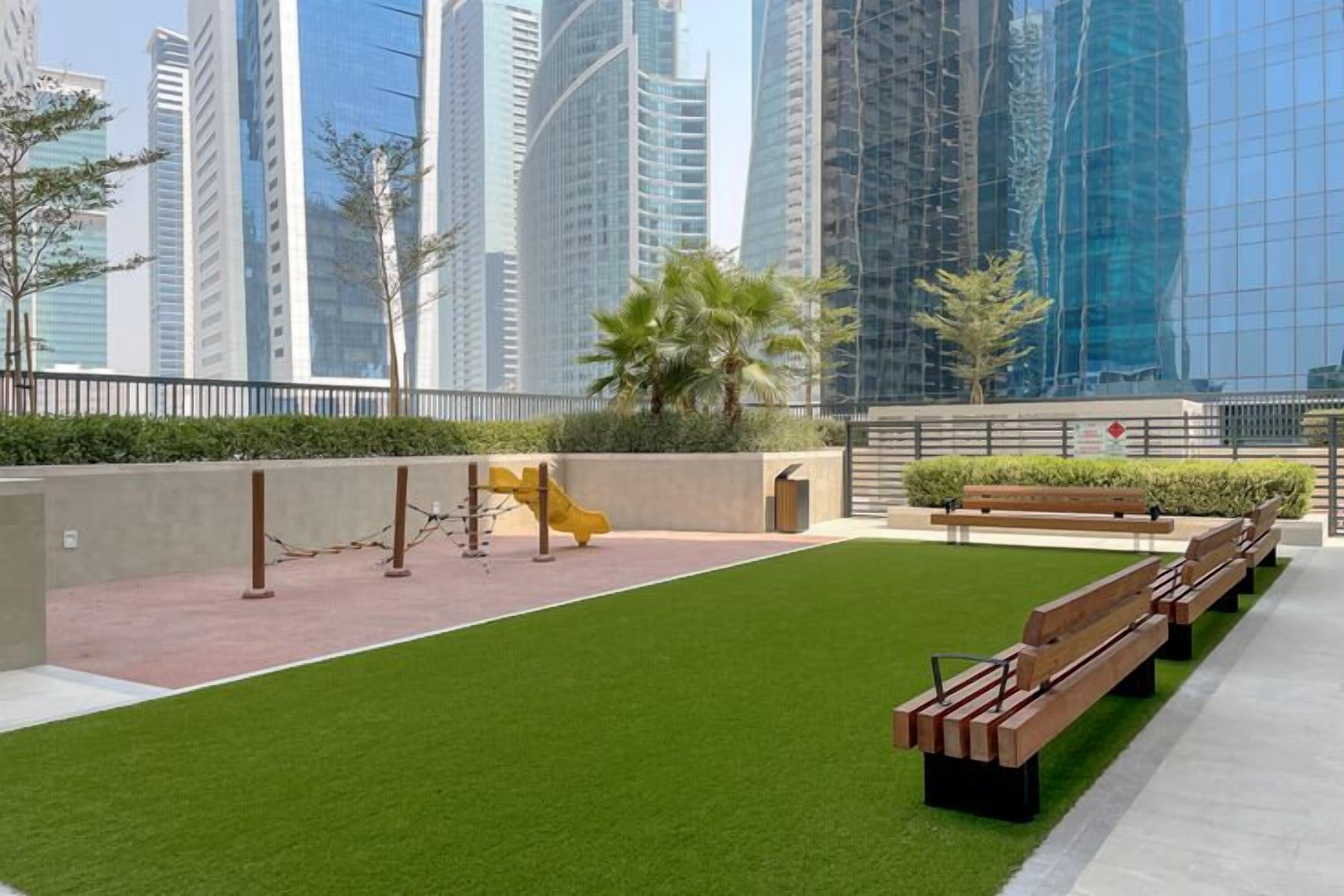 Un parc urbain moderne doté de gazon synthétique, d’une aire de jeux et de bancs.