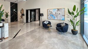 Eine moderne Lobby mit Marmorboden, zwei blauen Sesseln, einem großen abstrakten Gemälde und Zimmerpflanzen.