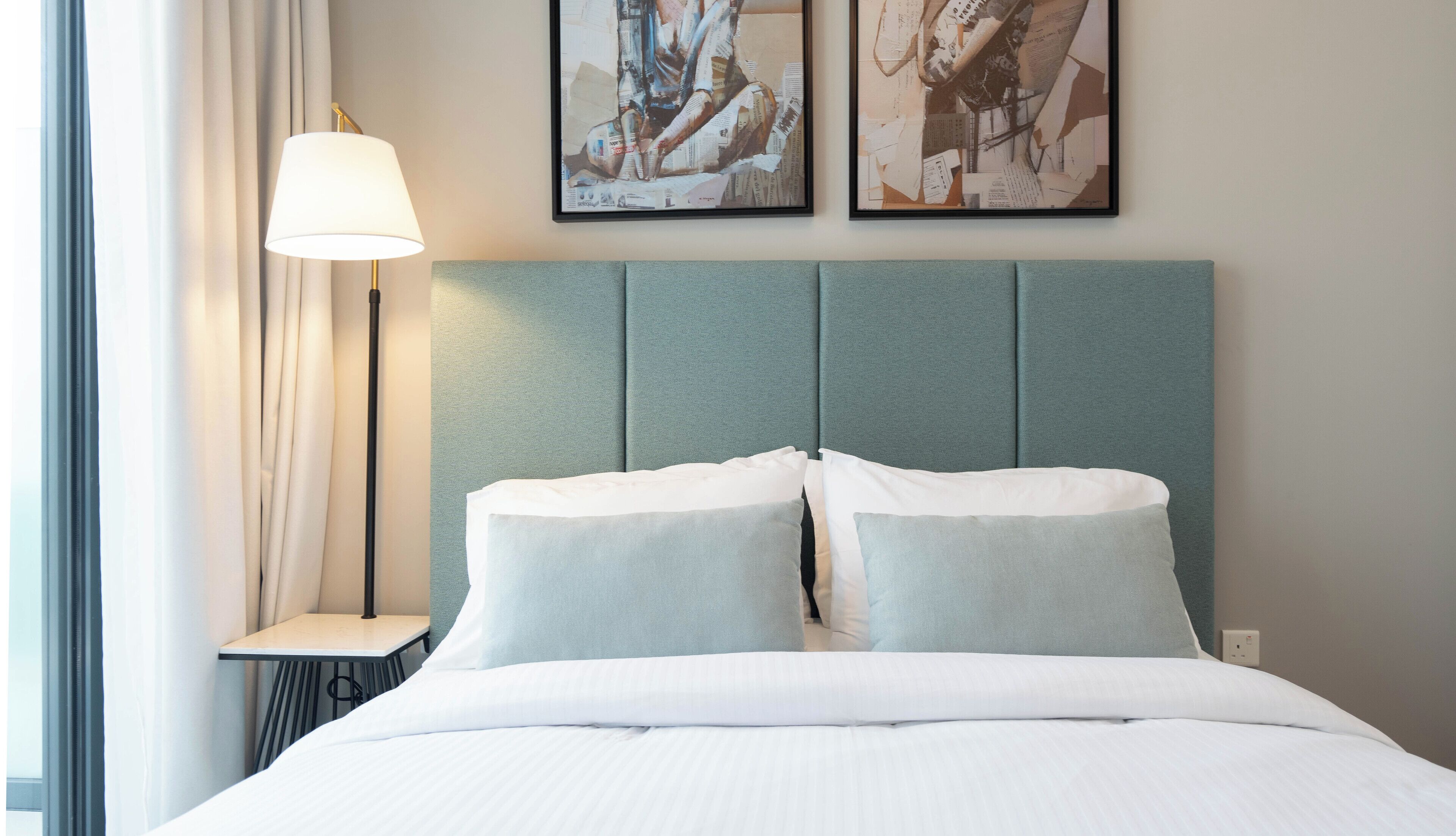 A hotel room with a bed, a nightstand, a lamp, and two wall art pieces.
