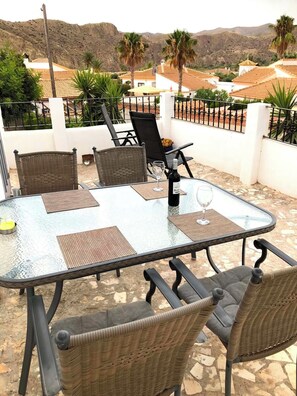 A glass-top table with wicker chairs, a bottle of wine, and a glass on a patio with a view of hills and palm trees. - 2-Bedroom Apartment with Terrace (Arboleas, La Perla)