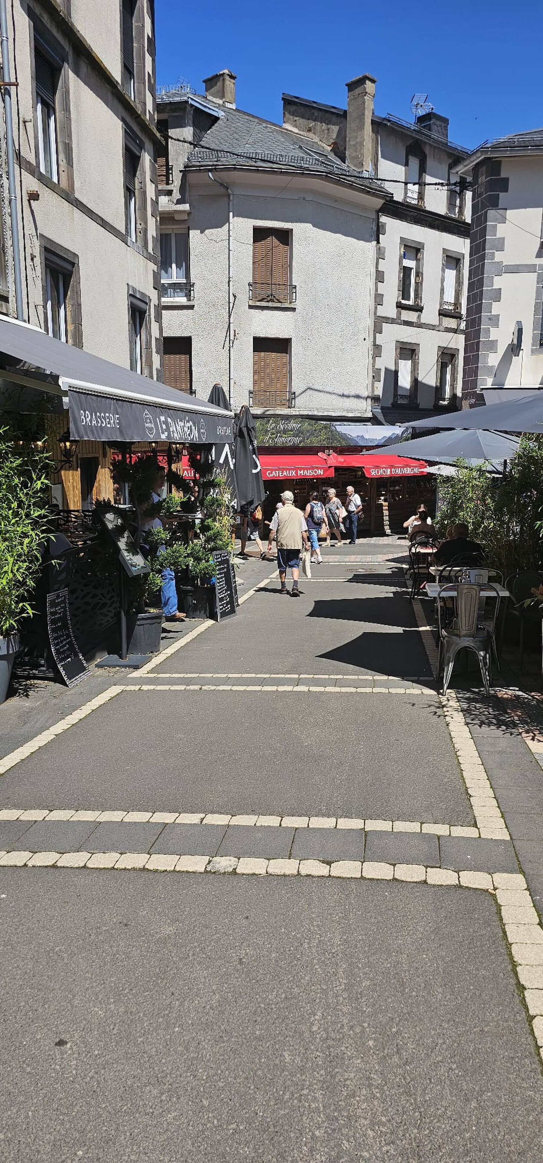 A street with shops and outdoor seating, featuring a sign for 'Le P'tit P'tit'.