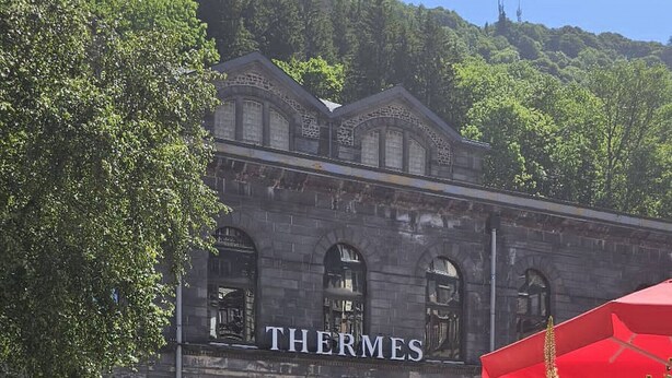Un edificio con el nombre "THERMES" en su fachada, rodeado de un jardín con diversas flores y plantas.