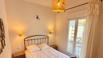 A bedroom with a bed, two wall-mounted lamps, a ceiling light, a window with a view of the outside, and a curtain.