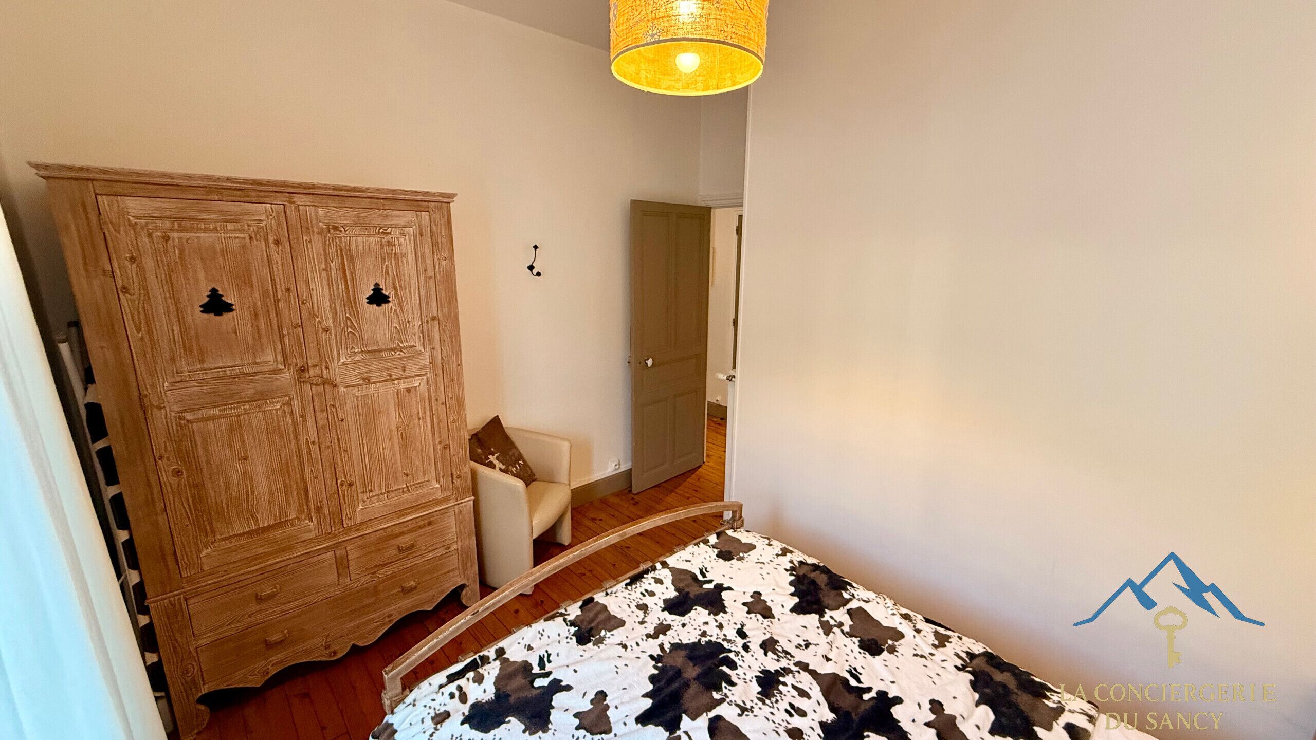 A bedroom with a wooden wardrobe, a bed with a cowhide cover, and a hanging light fixture.