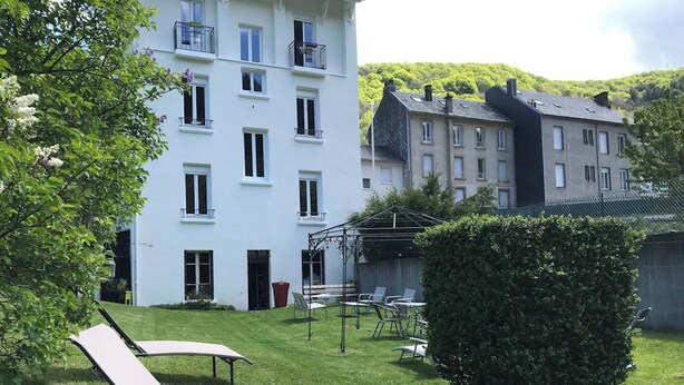 Un patio con un edificio blanco, mobiliario exterior y un seto cuidado.