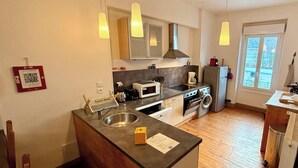 Una cocina moderna con una isla central, pileta de acero inoxidable y microondas. Hay luces colgantes, una ventana y una puerta que da al exterior.