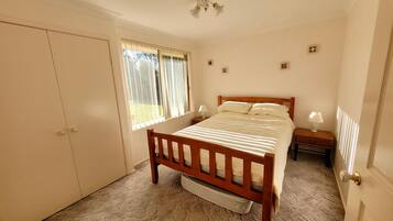 A bedroom with a wooden bed, two bedside tables with lamps, a wardrobe, and a window with blinds.