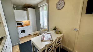 A compact kitchen with a washing machine, a dining table with chairs, and a clock on the wall.