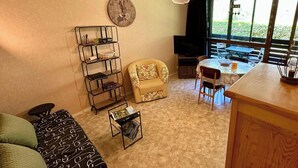 Una sala de estar acogedora con un sofá, una pequeña mesa de centro, una estantería, un televisor y un comedor con mesa y sillas.