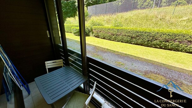 Un balcón con mesa y sillas, con vistas a un jardín cuidado y una valla.