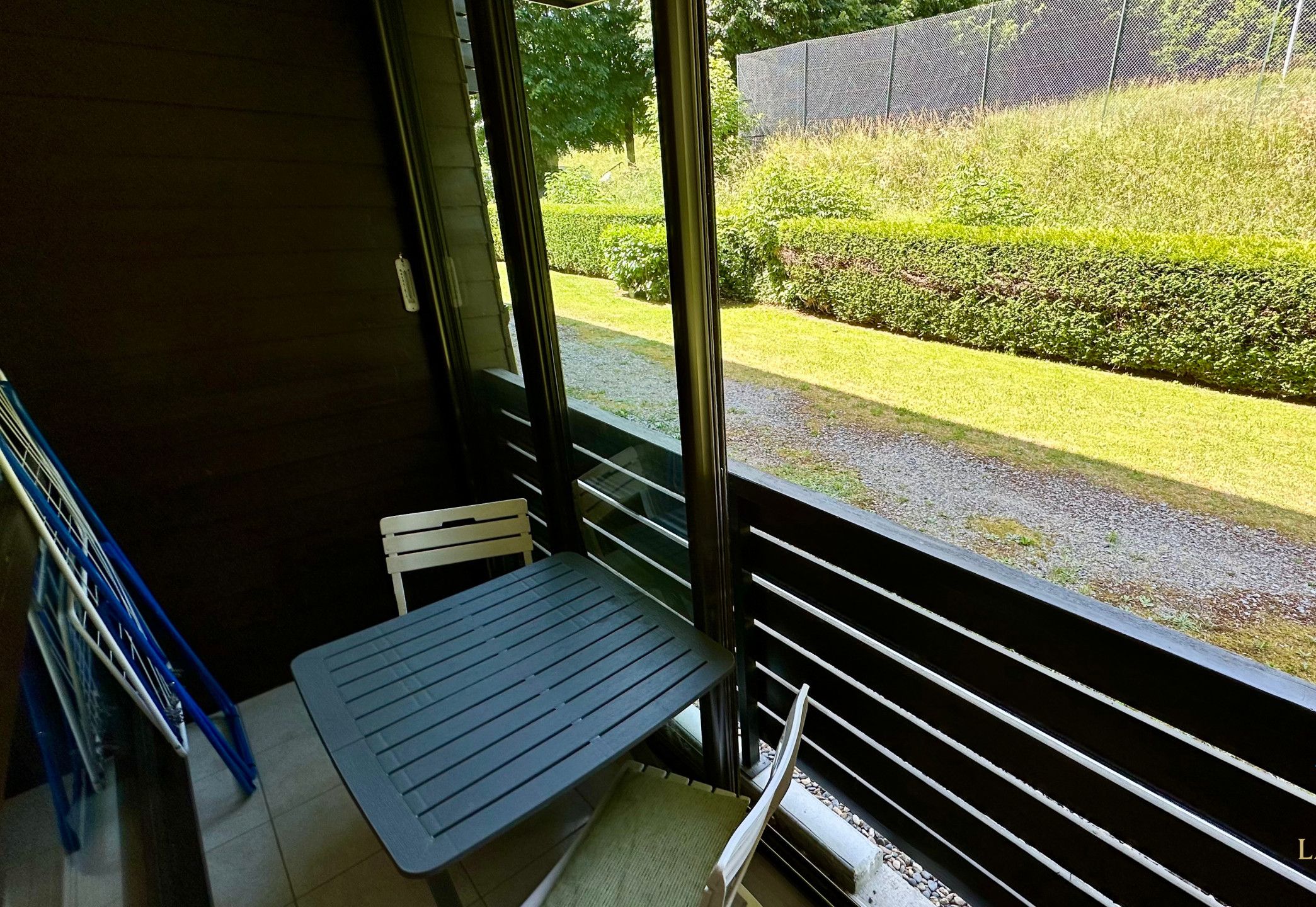 Uma varanda com mesa e cadeiras, com vista para um jardim bem cuidado e uma cerca.