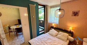 A bedroom with a bed, bedside lamps, a window with curtains, a door leading to a balcony, and a small table with a chair. - Le Pradet A 781 - Mont Dore 4 pers (Mont-Dore)