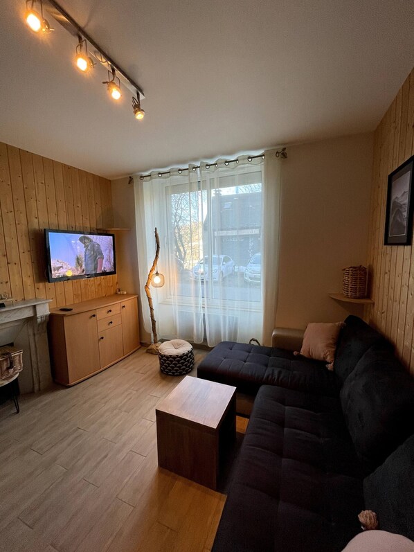 Ett mysigt vardagsrum med en mörk soffa, träskåp, en tv och ett fönster med gardiner.