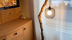 A wooden cabinet with drawers, a television mounted above it, and a unique branch-shaped floor lamp with a woven shade. - La Féessence boisée - 2/4 pers (Mont-Dore)