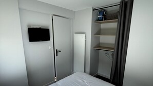 Une chambre d’hôtel avec un lit, un téléviseur fixé au mur, une armoire et une étagère sur laquelle se trouve un sac.