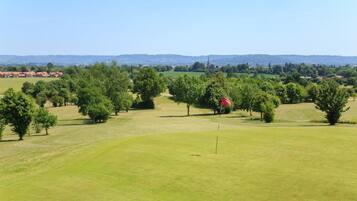 Un campo de golf con un mástil de bandera al frente, rodeado de árboles y zonas verdes abiertas.