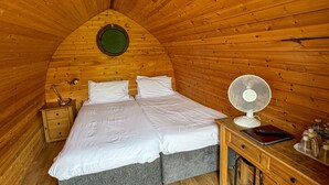 Kodikas huone, jossa on puupanelointi, sänky, työpöytä ja tuuletin.
