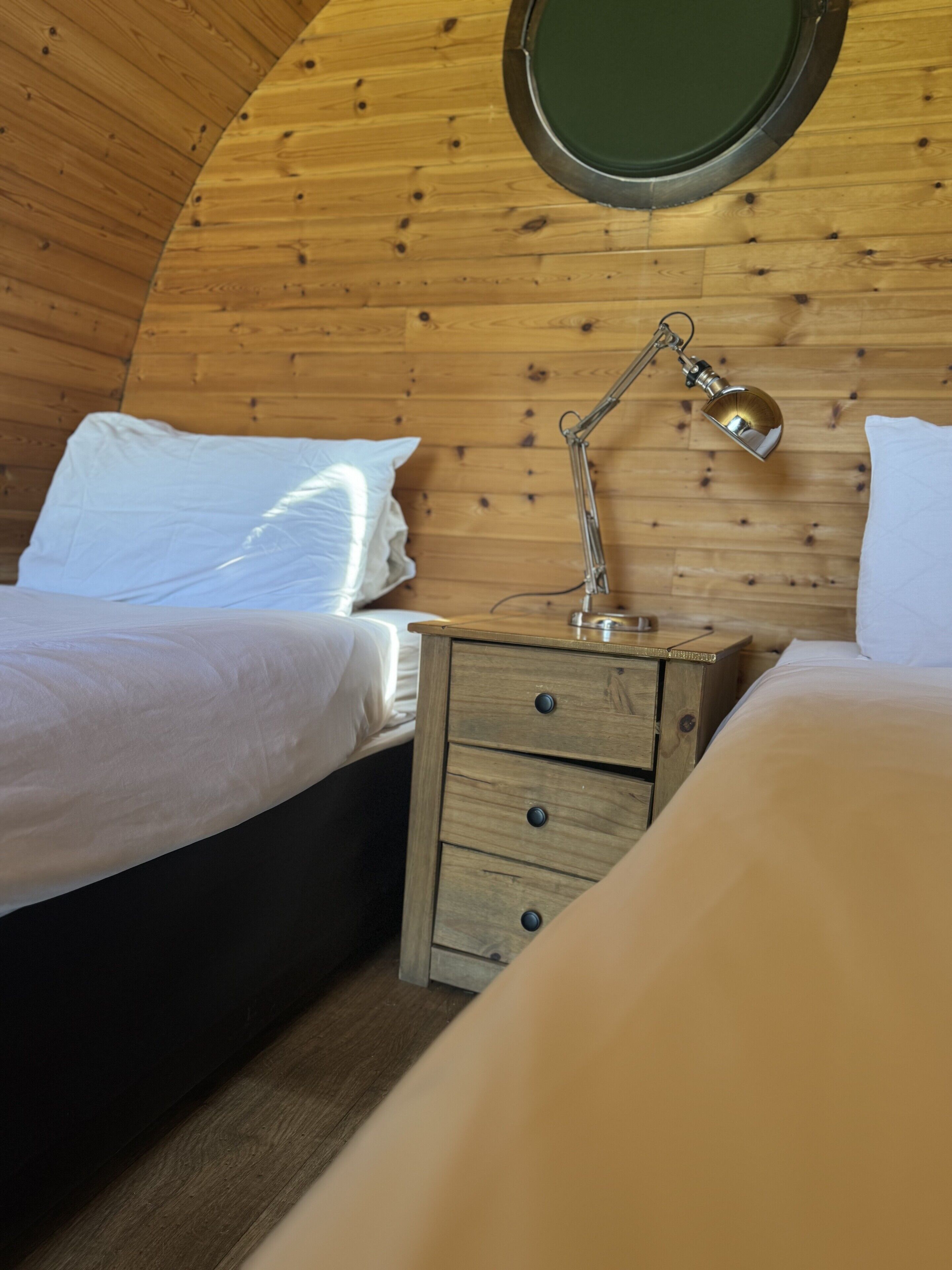 A cozy bedroom with a wooden bunk bed, a bedside table with a lamp, and a round mirror on the wall.