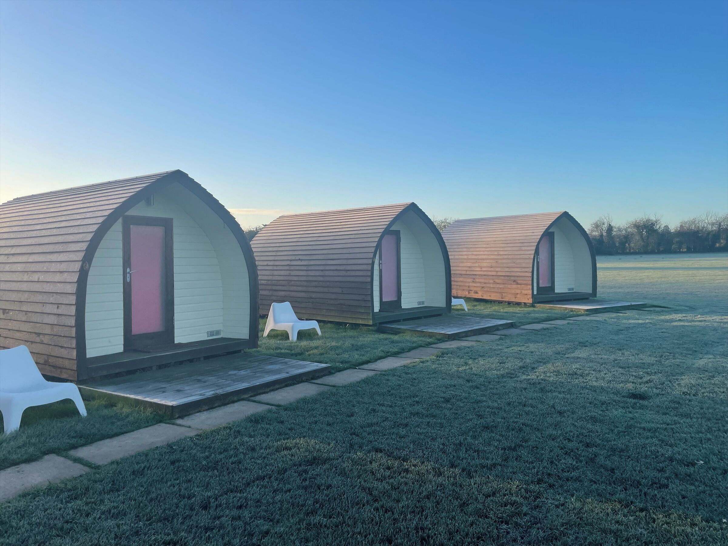 Three small, arched, single-room cabins with a grassy lawn and a clear sky.