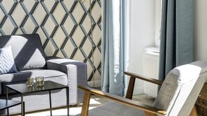 Een moderne woonkamer met een wand met geometrische patronen, een bank, een stoel, een bijzettafeltje en een raam met gordijnen.