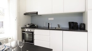 Een kleine keuken met witte kastjes, een zwart aanrecht en basisapparatuur, waaronder een fornuis, oven en koffiezetapparaat.