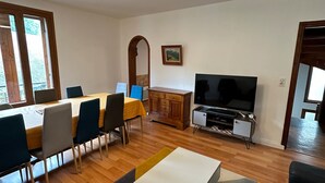 Una sala de estar moderna con comedor, suelo de madera, televisor de pantalla plana y un ventanal grande.