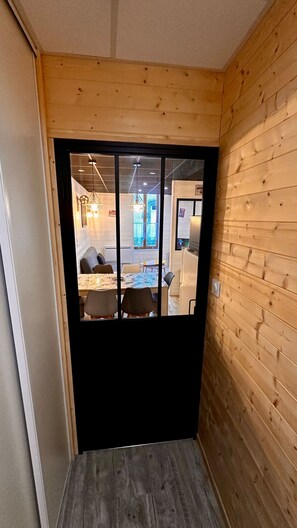 Ein Zimmer mit Holzvertäfelung und einer schwarzen Tür, die in einen Essbereich mit Tisch und Stühlen führt.