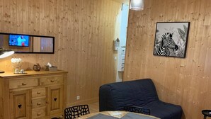 Una habitación con paneles de madera, una mesa redonda, sillas, un sofá, un televisor y un cuadro en la pared.