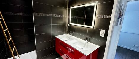 A bathroom with dark tiles, a white sink, a red vanity, and a mirror.