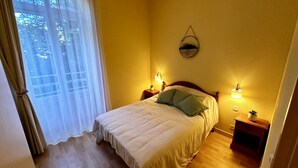 Une chambre à coucher avec un lit, deux lampes de chevet, un luminaire fixé au mur et une fenêtre avec des rideaux.