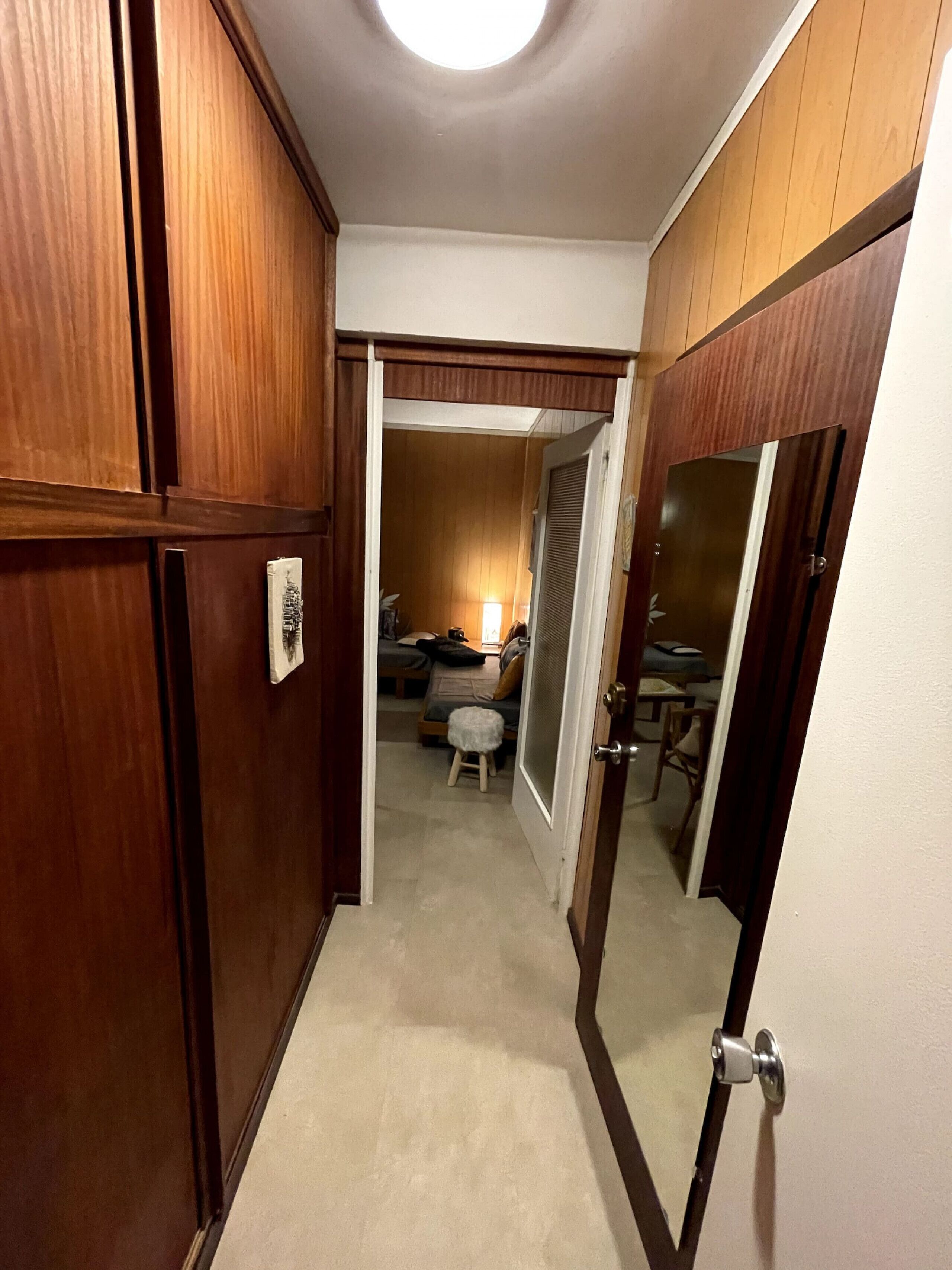 Ein Flur, der in ein Schlafzimmer mit Bett, Hocker und Nachttisch führt.