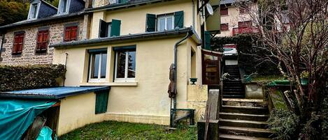 Una casa de dos pisos con fachada de piedra, un pequeño jardín y una escalera que conduce al piso superior.
