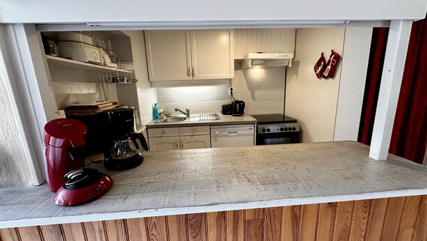 Una cocina compacta con armarios blancos, un fregadero, una estufa y una cafetera.