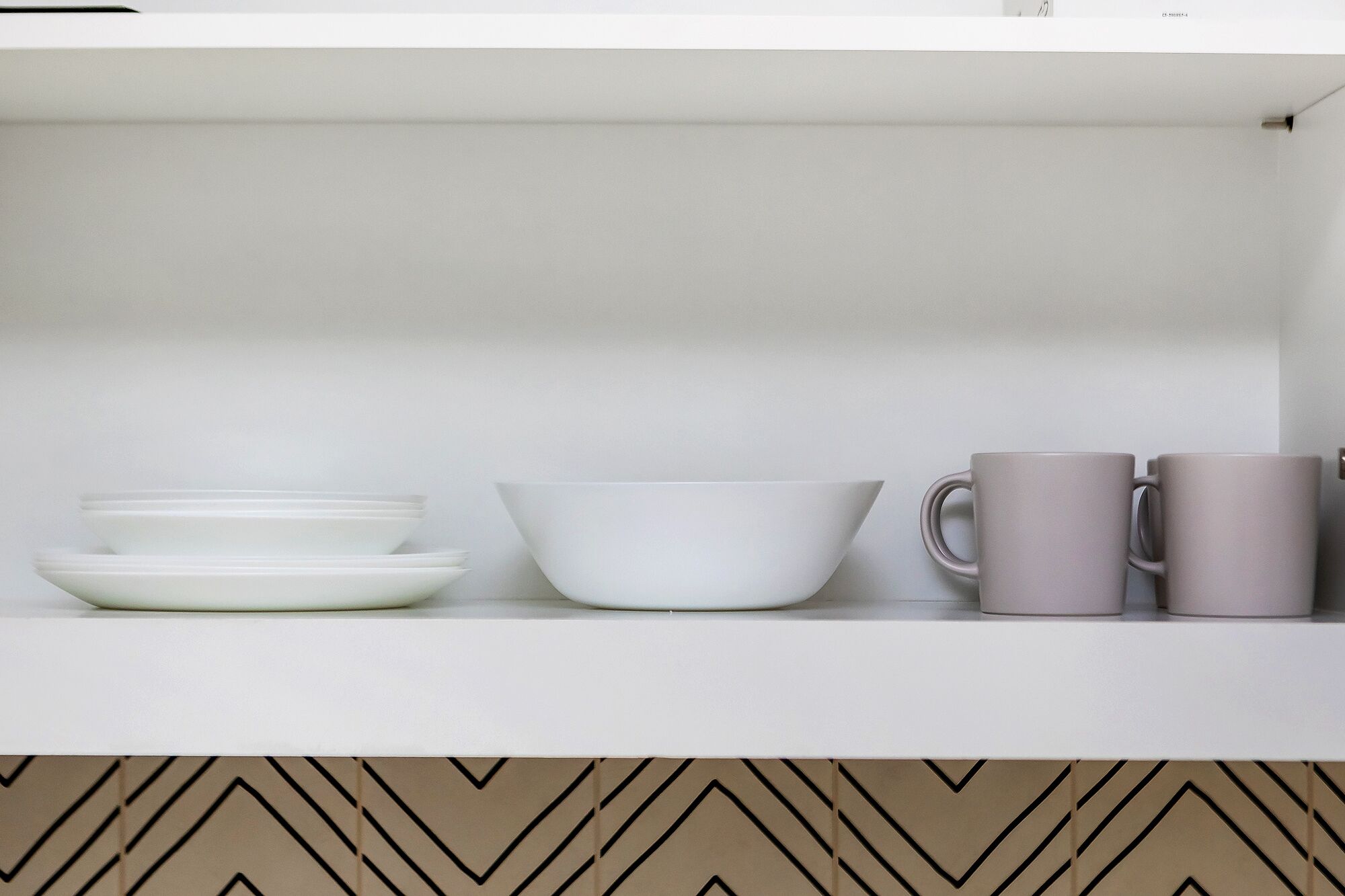Une étagère de cuisine avec des assiettes blanches, un saladier blanc et deux tasses grises.