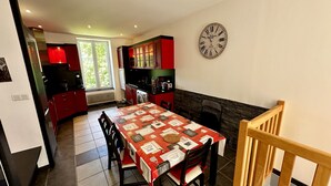 A dining area with a table set for four, a kitchen with red cabinets, a clock on the wall, and a fireplace. - Le Rocher - Le Mont Dore 6 pers (Mont-Dore)