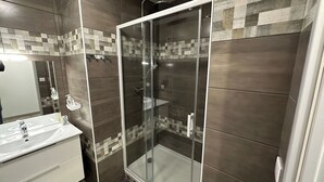 A modern bathroom with a glass-enclosed shower, a vanity with a mirror, and tiled walls. - Ruche 5 - Le Mont Dore 7 pers (Mont-Dore)