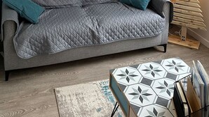 A living room with teal walls, a grey sofa, a geometric coffee table, and a wall-mounted abstract painting. - Ruche 5 - Le Mont Dore 7 pers (Mont-Dore)