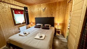 Une pièce aux murs lambrissés, avec un lit, deux lampes de chevet, une fenêtre ornée d’un rideau rouge et une tête de cerf accrochée au mur.
