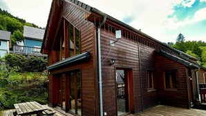 Une cabane en bois dotée d’une terrasse, de grandes fenêtres et d’une porte donnant sur un porche abrité.